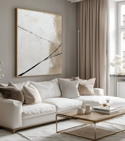 A large framed abstract wall art print with black brushstrokes on a beige and white background, hanging above a modern white sofa in a styled living room.