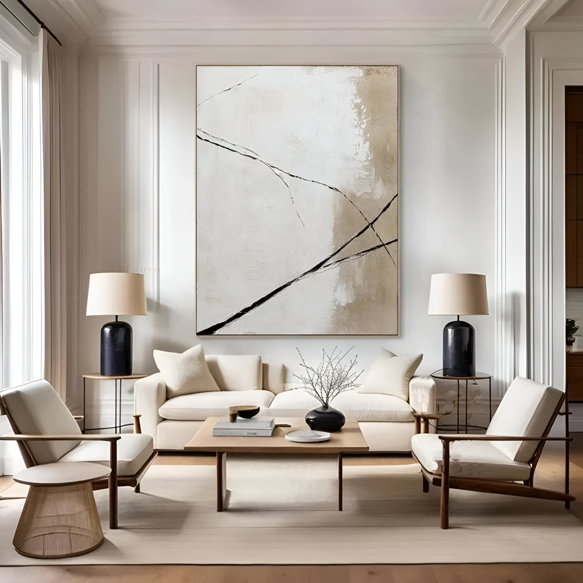A large abstract canvas print with black brushstrokes on a cream and beige background hangs on a white wall above a modern white sofa in a styled living room with two armchairs, side tables, and lamps.